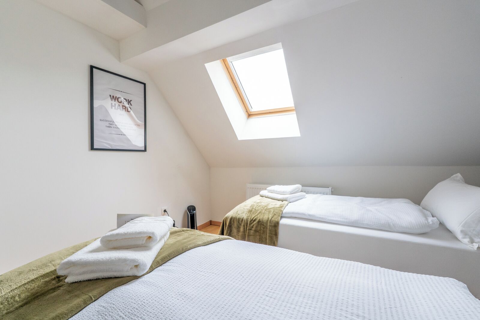 A room with two beds, a skylight, a framed quote on the wall, and a radiator.