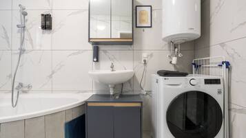 A modern bathroom with a bathtub, sink, mirror, and a washing machine.