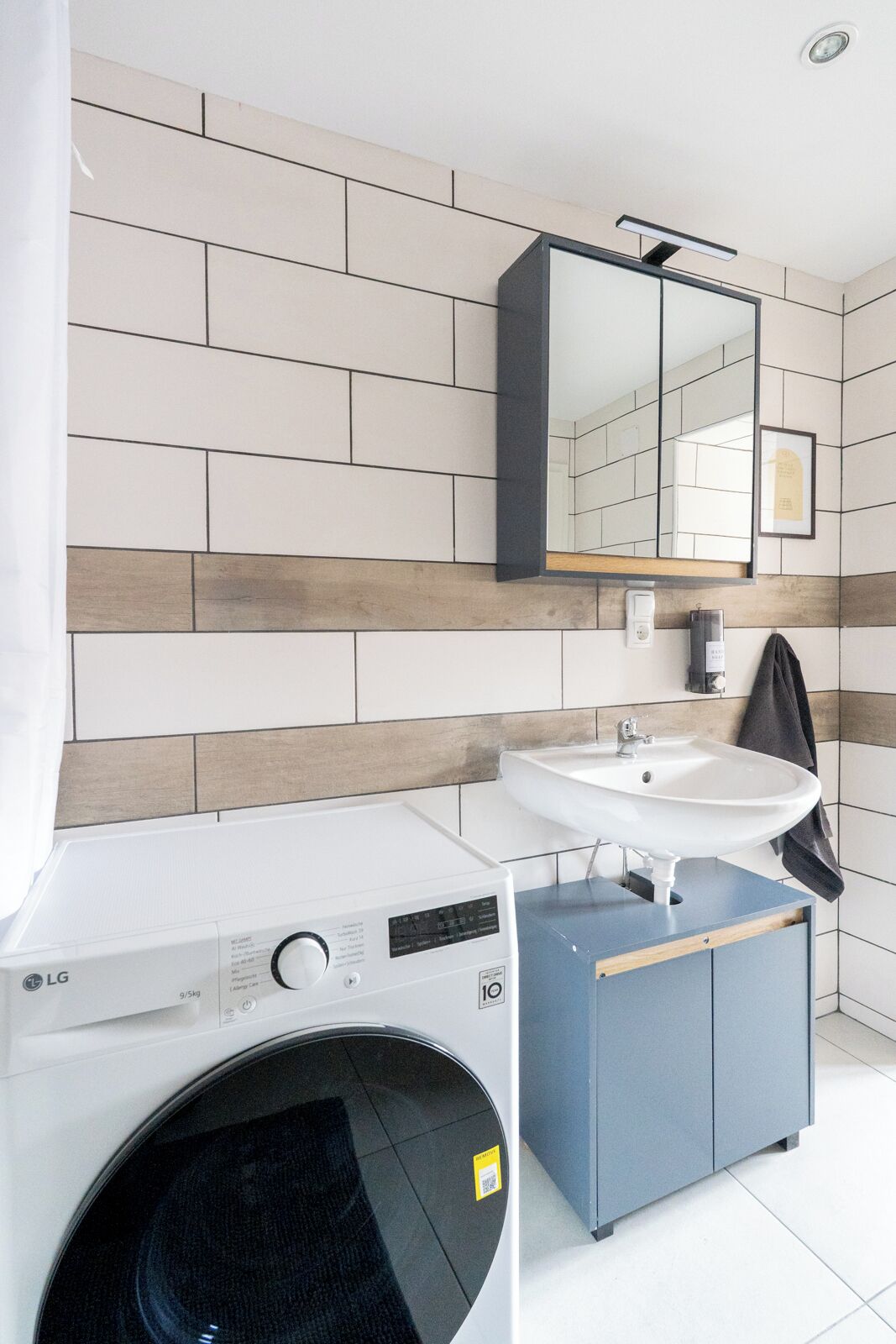 A modern bathroom with a washing machine, sink, and a mirror above the sink.