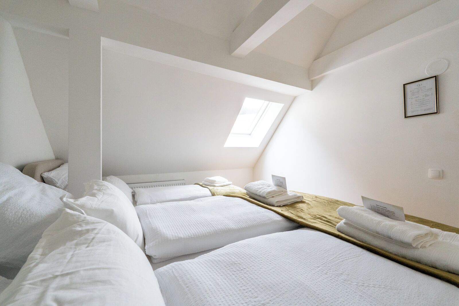 Una habitació amb dos llits, un sobrecap de fusta, un fanal i un certificat emmarcat a la paret.