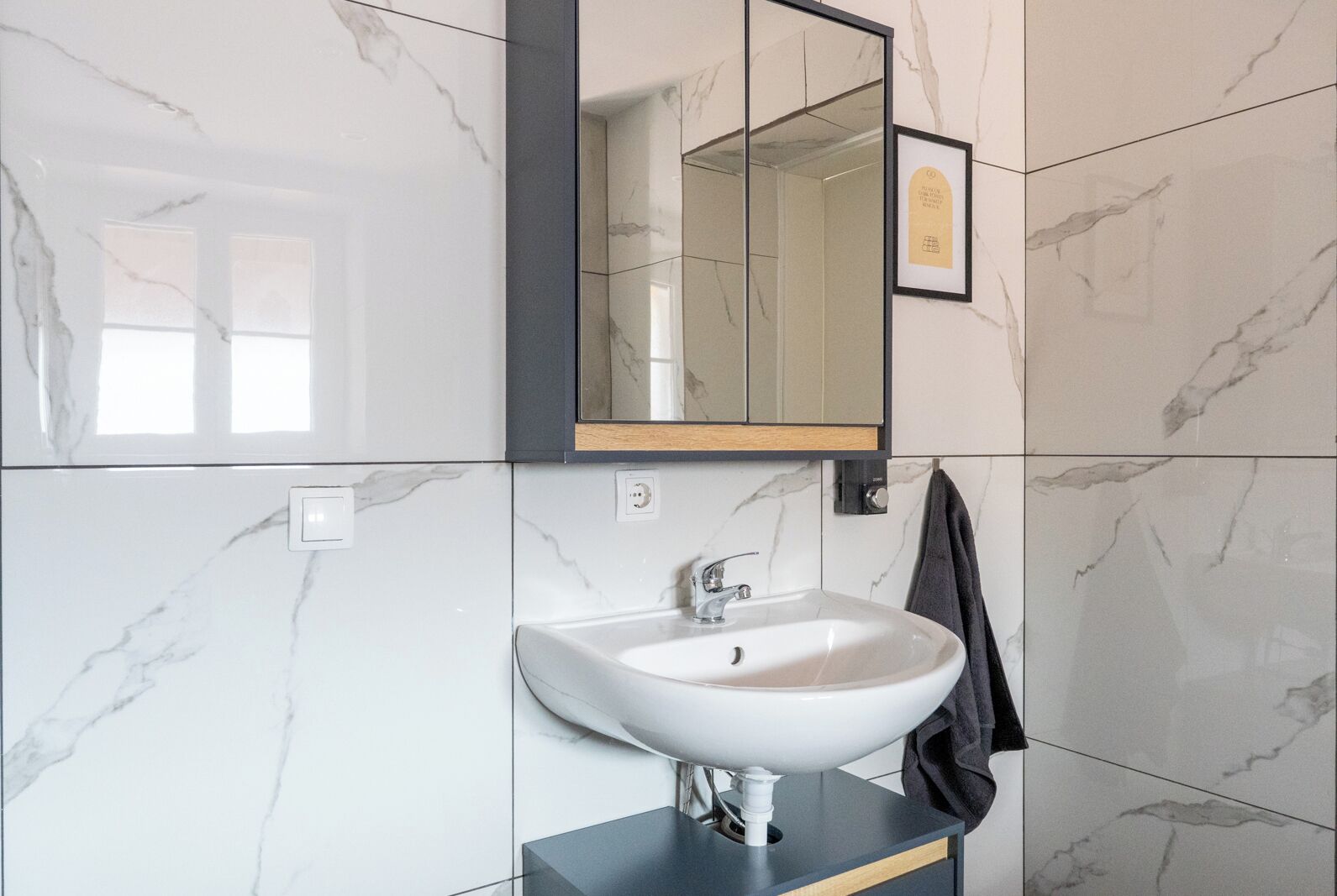 Un baño con lavamanos de mármol blanco, un espejo y un certificado enmarcado en la pared.