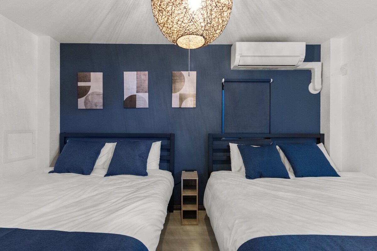 A hotel room with two beds, a ceiling light fixture, and an air conditioning unit.