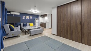 Ein modernes Wohnzimmer mit Sofa, Hocker und Couchtisch, einer Küchenzeile und einem großen Kleiderschrank.