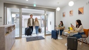 Eine moderne Hotelhalle mit einer Rezeption, Glastüren, einer Sitzecke mit Tischen und einer Kaffeemaschine.
