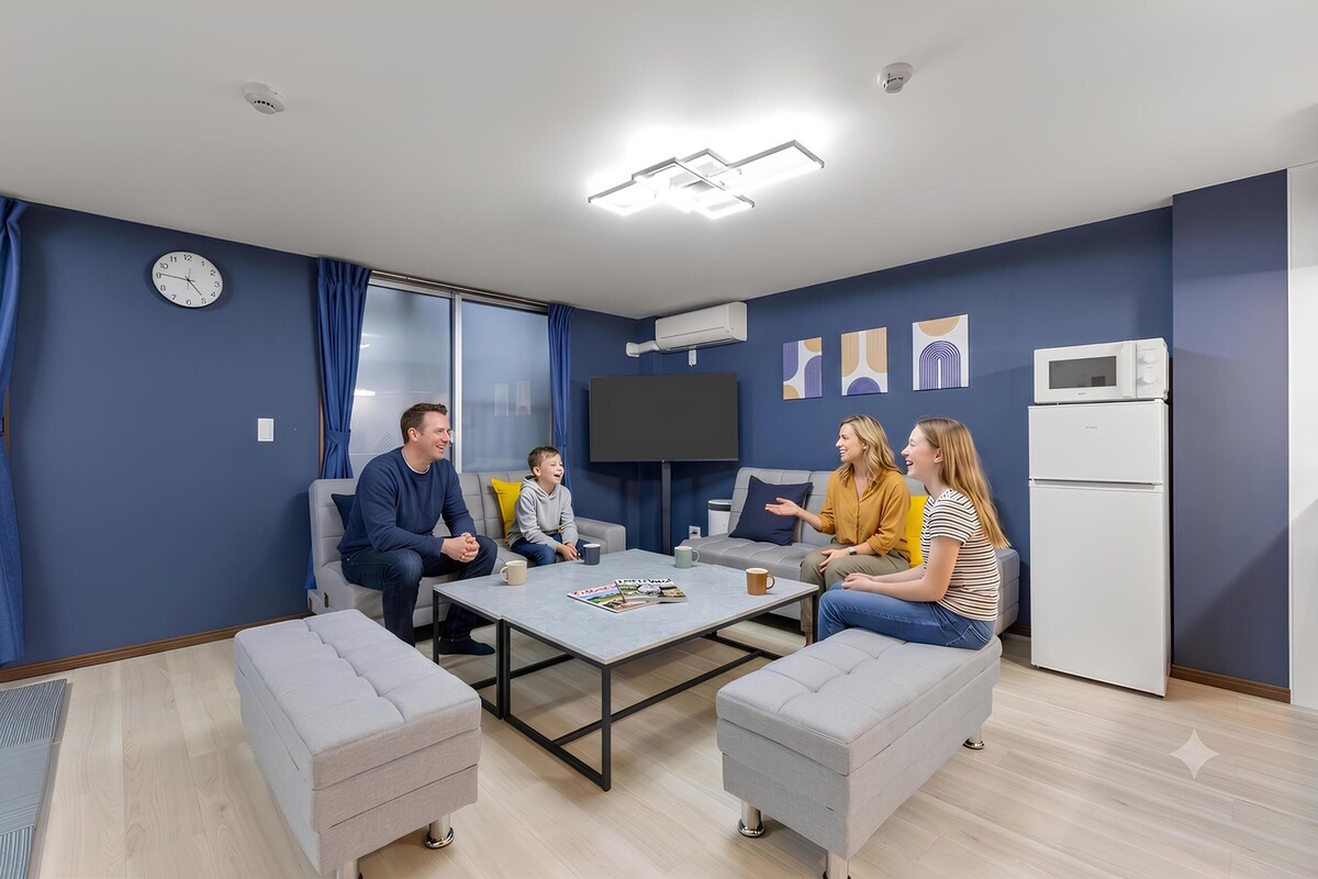 A modern living room with a flat-screen TV, a coffee table, and a refrigerator.
