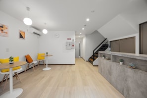 A modern interior with a reception desk, seating area with yellow chairs, a staircase, and a clock on the wall.