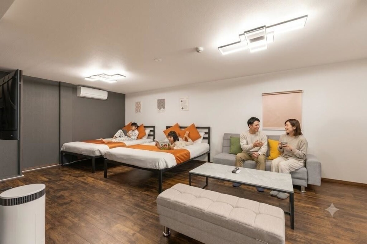 A modern hotel room with two beds, a sofa, a coffee table, and a standing heater.