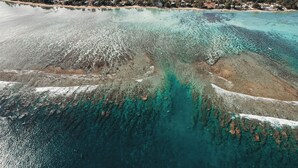 Una vista aerea di una zona costiera con acque turchesi cristalline, spiagge sabbiose e una zona residenziale densamente popolata sullo sfondo.