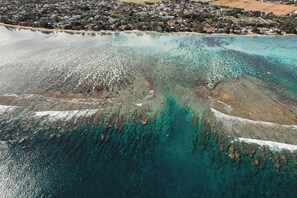 Eine Vogelperspektive zeigt eine Küstenregion mit klarem türkisblauem Wasser, Sandstränden und einer dicht besiedelten Wohngegend im Hintergrund.