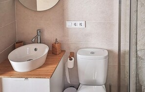 A bathroom with a white sink, wooden countertop, and a toilet. There is a mirror above the sink and a shower curtain to the right.