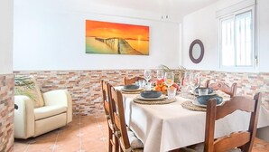 Un comedor con una mesa dispuesta para cuatro, un cuadro de un atardecer en la pared y una ventana con vistas al exterior.