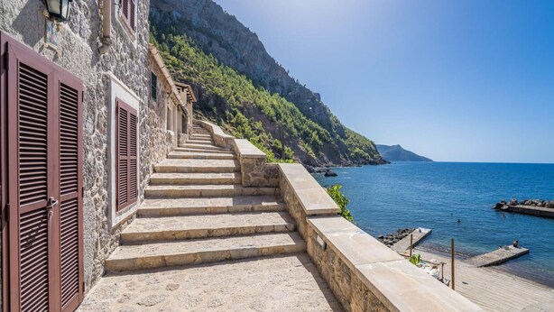 Eine Steintreppe führt zu einem Strand mit freiem Blick auf das Meer und eine felsige Klippe.
