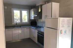 A kitchen with white cabinets, a gas stove, a refrigerator, and a window with a view of trees. - Classy Holiday Home in Santa Cristina d'Aro (Santa Cristina d'Aro)