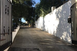 Ein schmaler Betonweg, begrenzt von weißen Mauern und einem Metallgitter, der zu einem Gebäude führt.