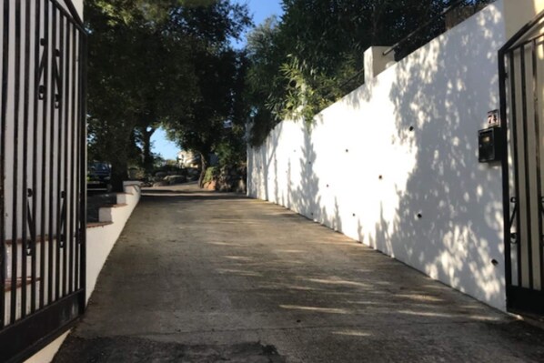 A narrow concrete pathway flanked by white walls and a metal gate, leading to a building. - Classy Holiday Home in Santa Cristina d'Aro (Santa Cristina d'Aro)