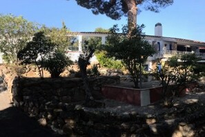 A stone retaining wall with a small garden area, a white building with a balcony, and a clear blue sky. - Classy Holiday Home in Santa Cristina d'Aro (Santa Cristina d'Aro)