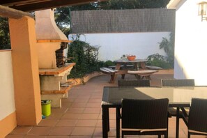 An outdoor patio with a grill, a table with chairs, and a small round table with a bowl. - Classy Holiday Home in Santa Cristina d'Aro (Santa Cristina d'Aro)
