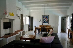 A living room with a black sofa, a wooden coffee table, a TV mounted on the wall, a dining area with a table and chairs, and a fireplace with a TV. - Holiday Home near Santa Cristina Forest (Santa Cristina d'Aro)