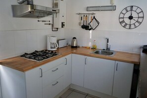 A kitchen with white cabinets, a wooden countertop, a gas stove, a coffee maker, a kettle, a sink, and a wall-mounted clock. - Holiday Home near Santa Cristina Forest (Santa Cristina d'Aro)
