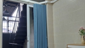 A room with a staircase, a blue curtain, a wooden chair, and a vase with flowers. - Omeli Homestay (Hanoi)