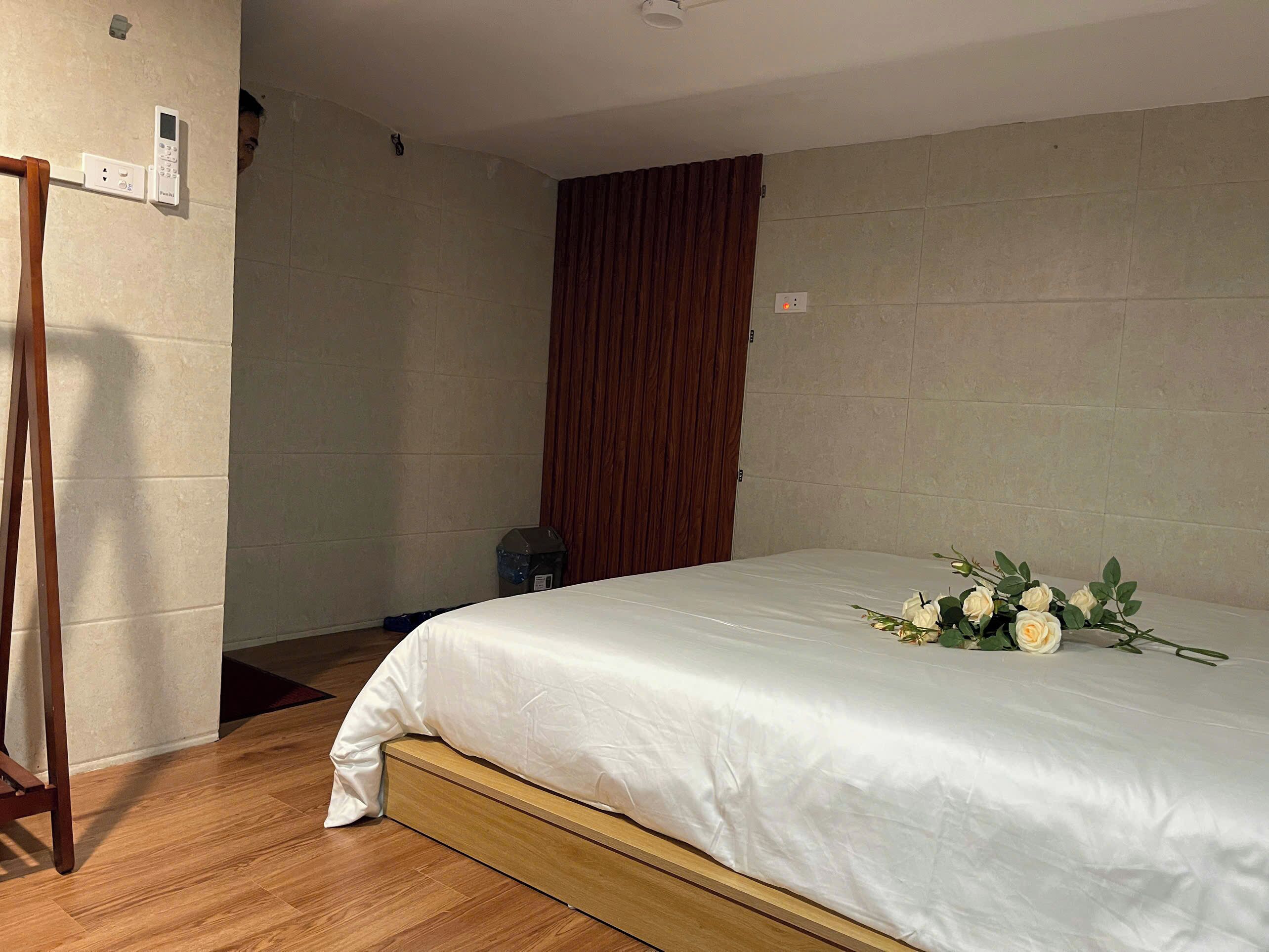 Ein Schlafzimmer mit einem hölzernen Bettgestell, einer weißen Bettdecke und einem Strauß weißer Blumen auf dem Bett.