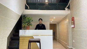 A hotel reception area with a staircase, a potted plant, a wooden stool, and a red fire alarm on the wall. - Omeli Homestay (Hanoi)