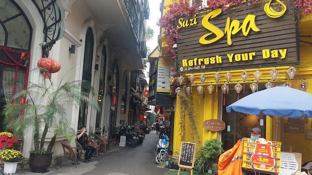 A narrow street with a yellow building featuring a sign that reads 'Suzi Spa Refresh Your Day.' - Omeli Homestay (Hanoi)