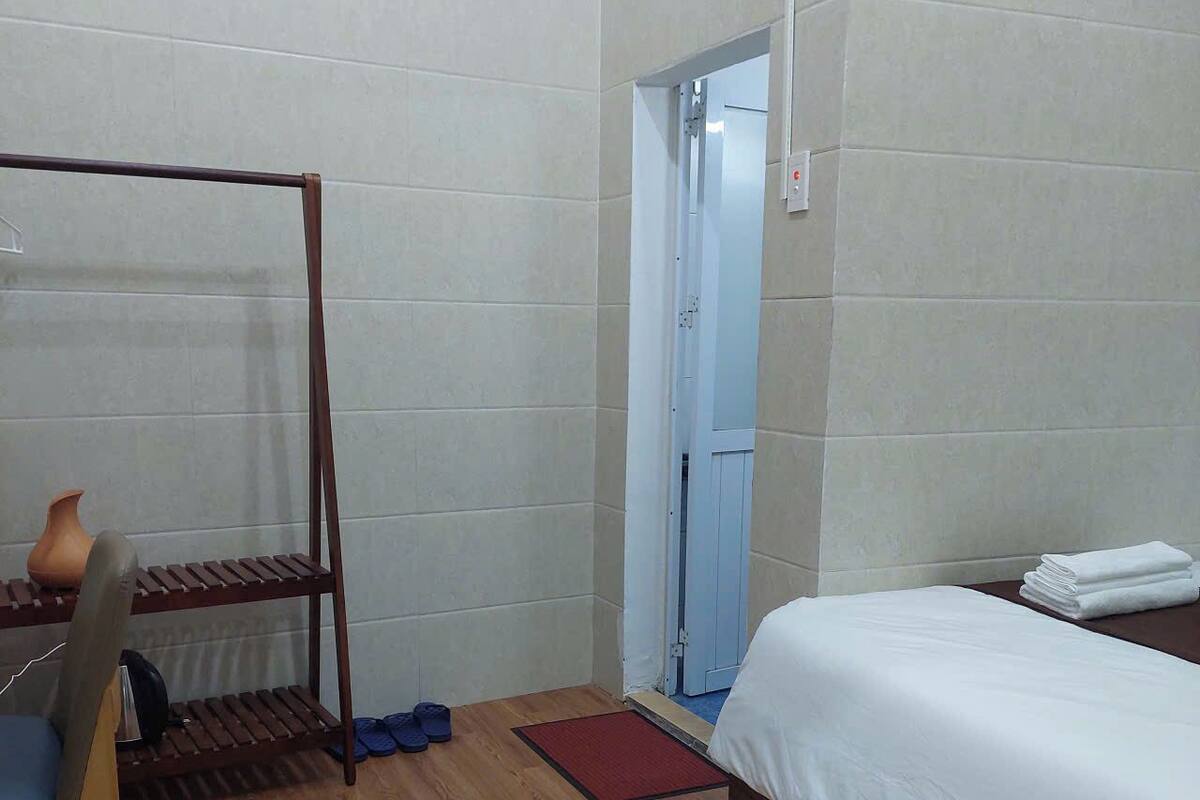 A bedroom with a bed, a wooden chair, a shelf with a vase, and a door leading to another room.