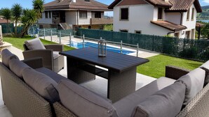 Une terrasse extérieure aménagée avec des meubles en osier, une piscine et une vue sur les maisons voisines.