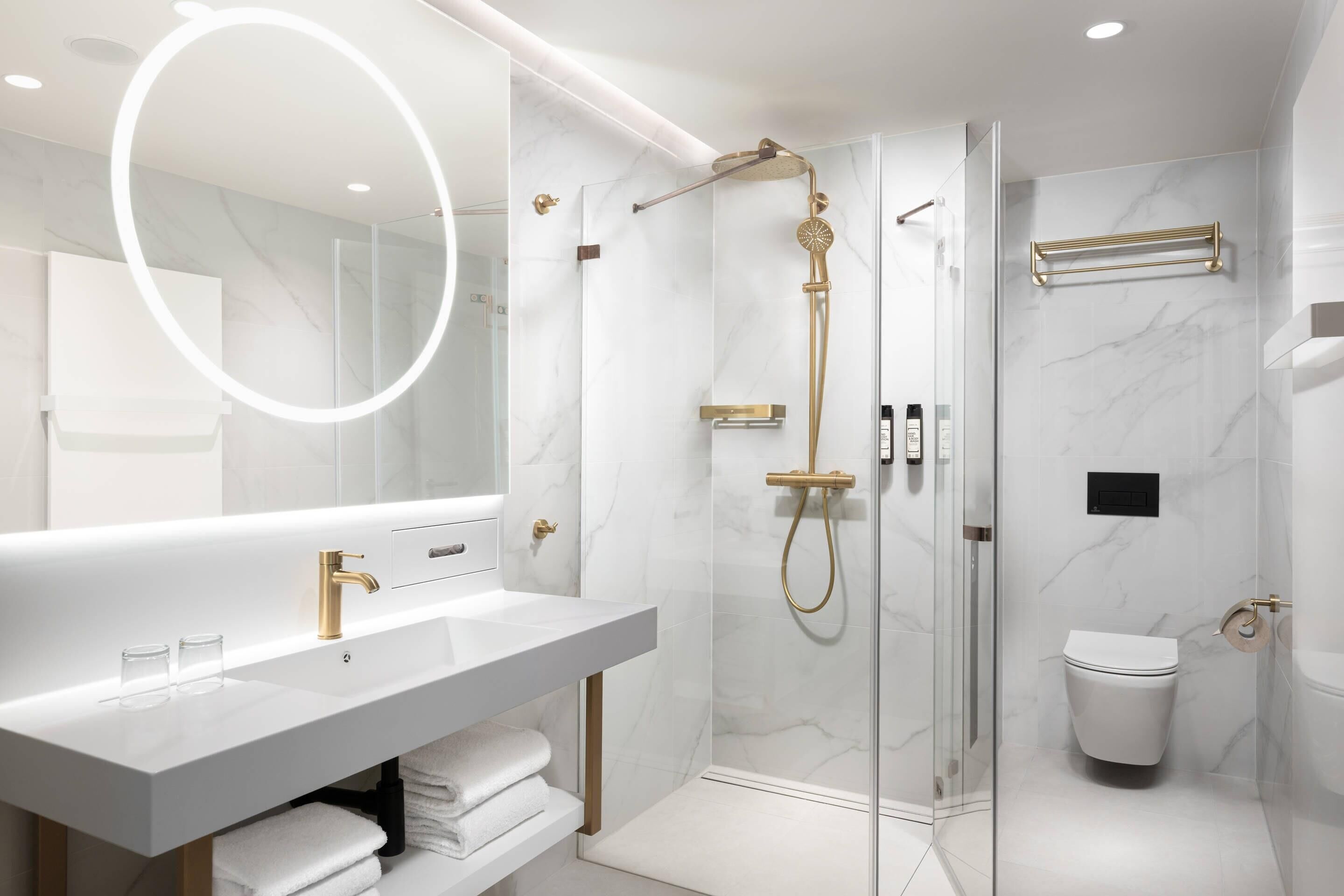 A modern bathroom with a glass-enclosed shower, a white vanity with gold fixtures, and a large mirror.