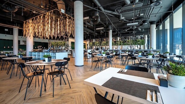 Un vaste espace intérieur doté de nombreuses tables et chaises, de grandes fenêtres et de conduits apparents.