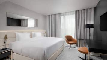 A modern hotel room with a large bed, a desk, a chair, and a TV.