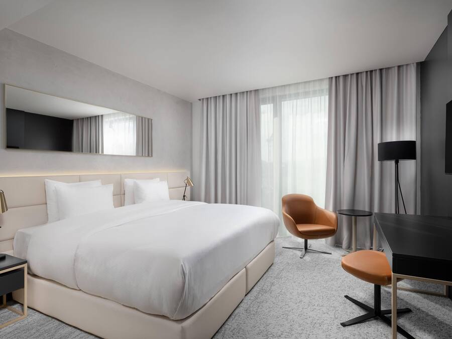 A modern hotel room with a large bed, a desk, a chair, and a TV.