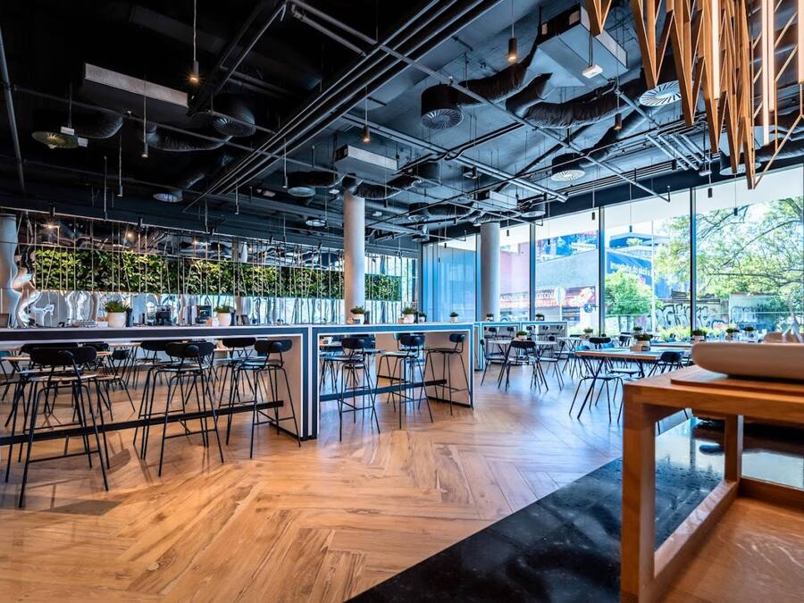 A modern cafe interior with high ceilings, exposed ductwork, and a mix of bar and dining areas.