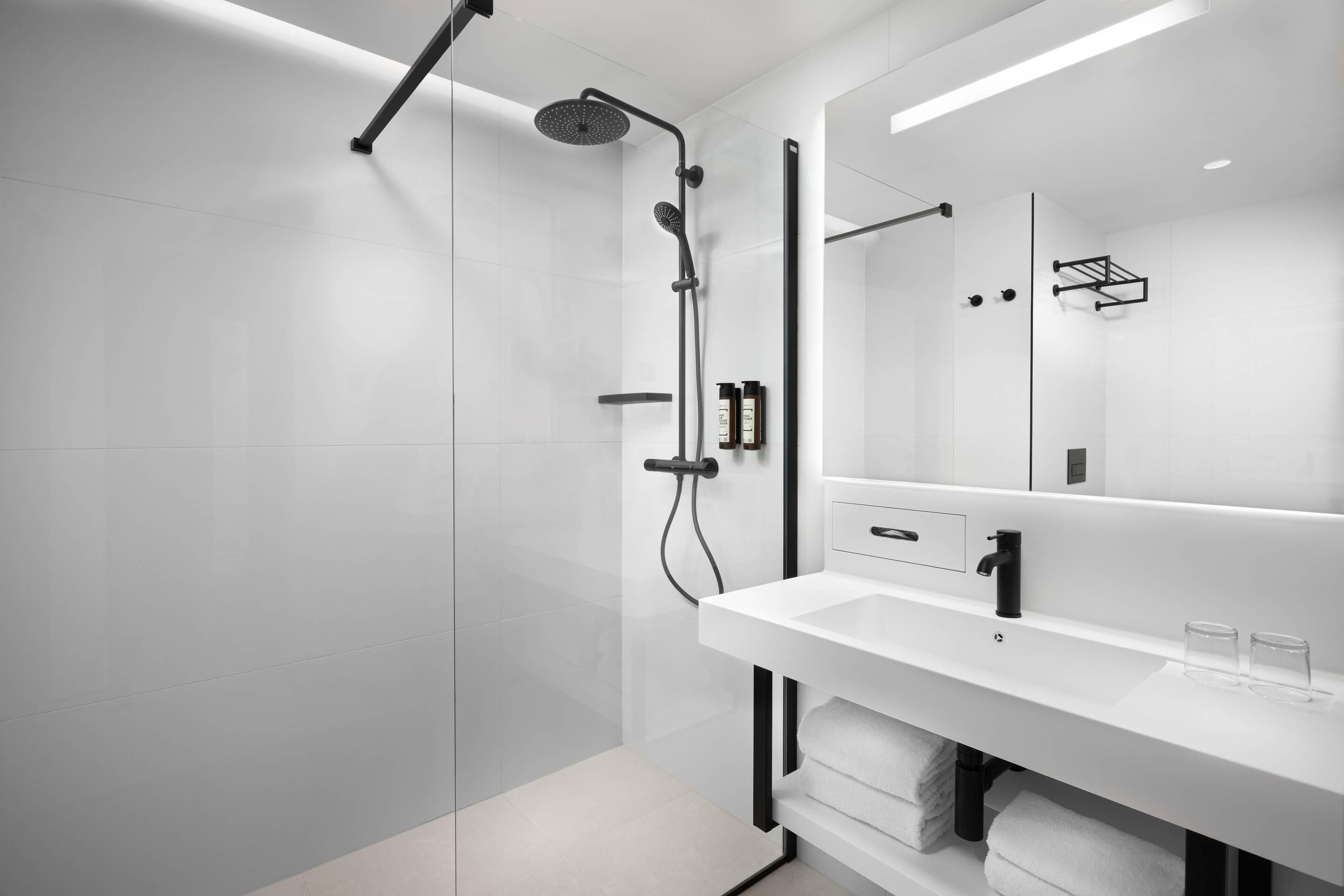 Ein modernes Badezimmer mit einer Glasdusche, einem weißen Waschbecken und einem großen Spiegel.