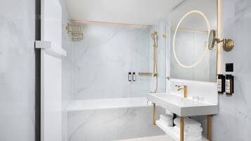 A modern bathroom with a white marble floor, a freestanding bathtub, a vanity with a gold faucet, and a large mirror with a gold frame.