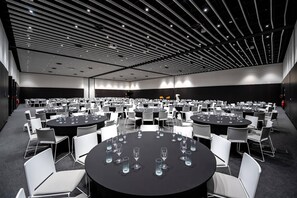Une grande salle de conférence dotée de nombreuses tables rondes et de chaises, d’un plafond haut avec un éclairage linéaire et d’une palette de couleurs neutres.