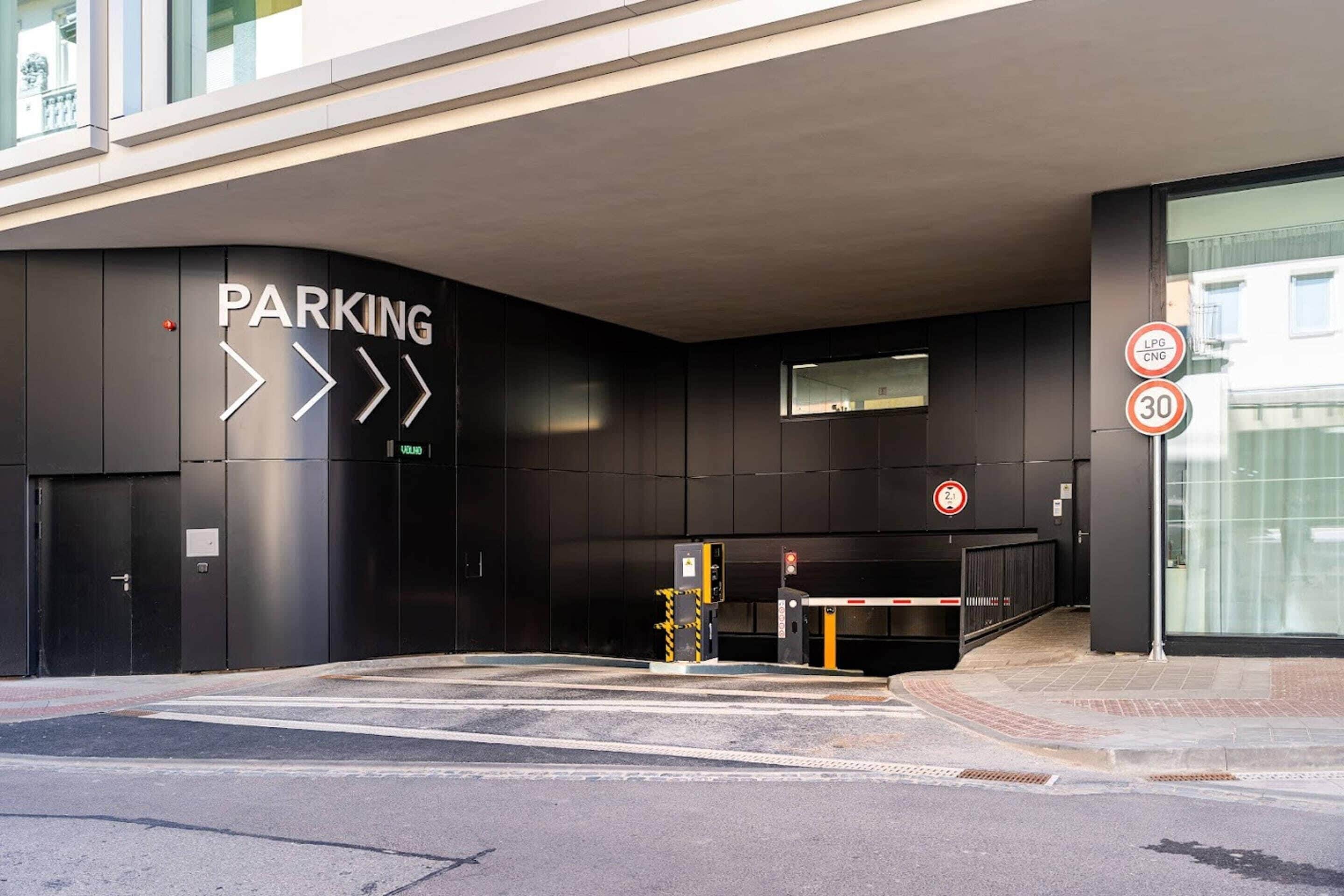 A modern building entrance with a parking sign, a speed limit sign, and a pedestrian crossing.