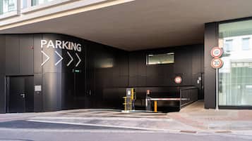 A modern building entrance with a parking sign, a speed limit sign, and a pedestrian crossing.