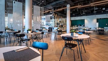 Un espacio interior amplio con varias mesas y sillas, ventanas grandes y un diseño moderno de techo industrial.