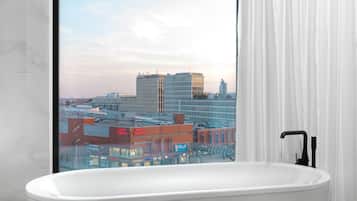 Un baño moderno con una bañera independiente, un ventanal con cortinas y vistas a un paisaje urbano.