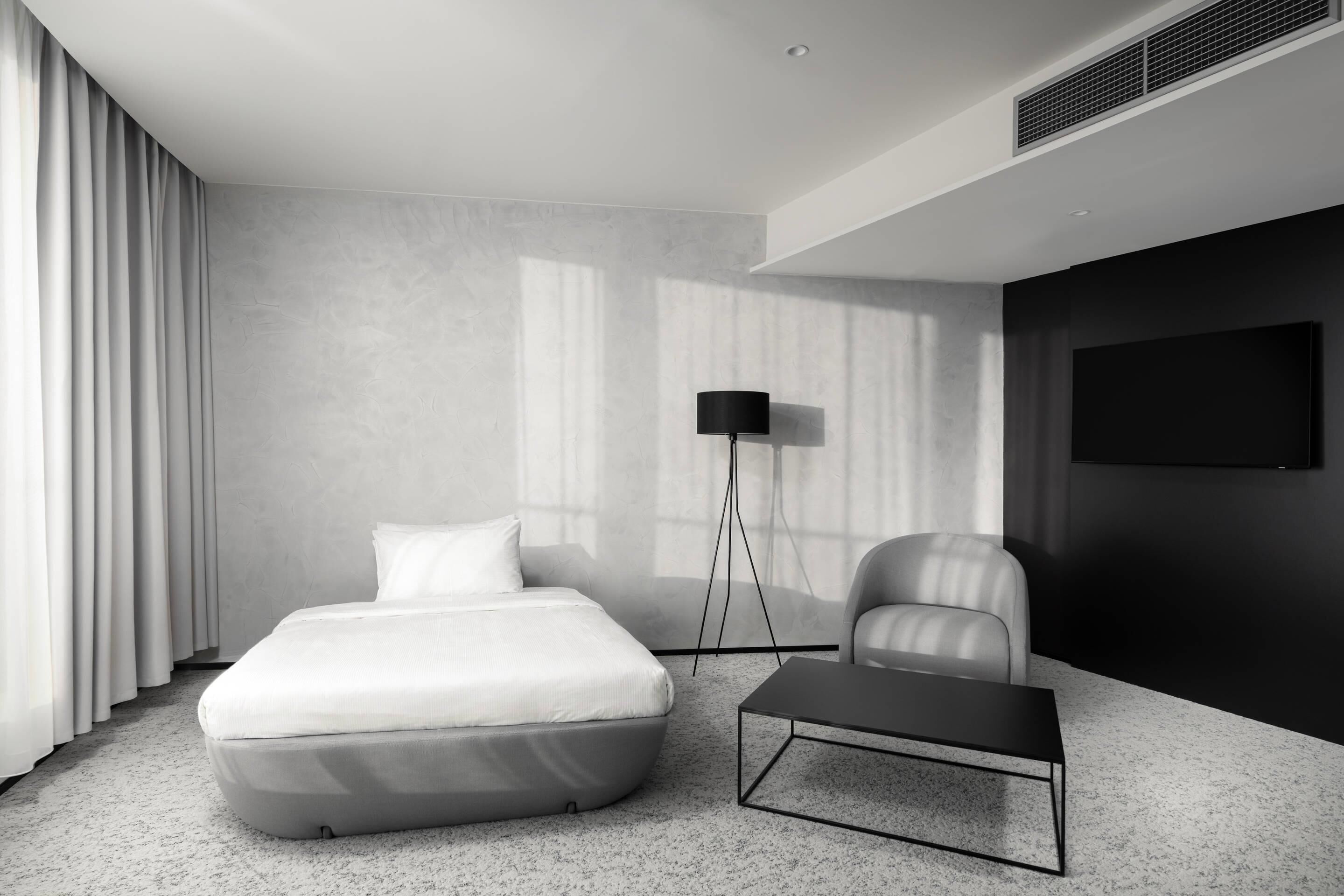 Habitación de hotel moderna con una cama, un escritorio, una silla, una lámpara de pie y un televisor en la pared.