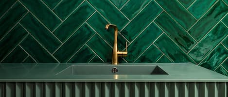 Un bagno con un lavandino moderno, un rubinetto dorato e una parete decorata con un motivo a spina di pesce verde.