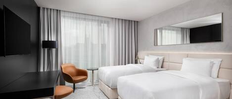 A hotel room with two beds, a desk, a chair, a small table, and a large mirror.