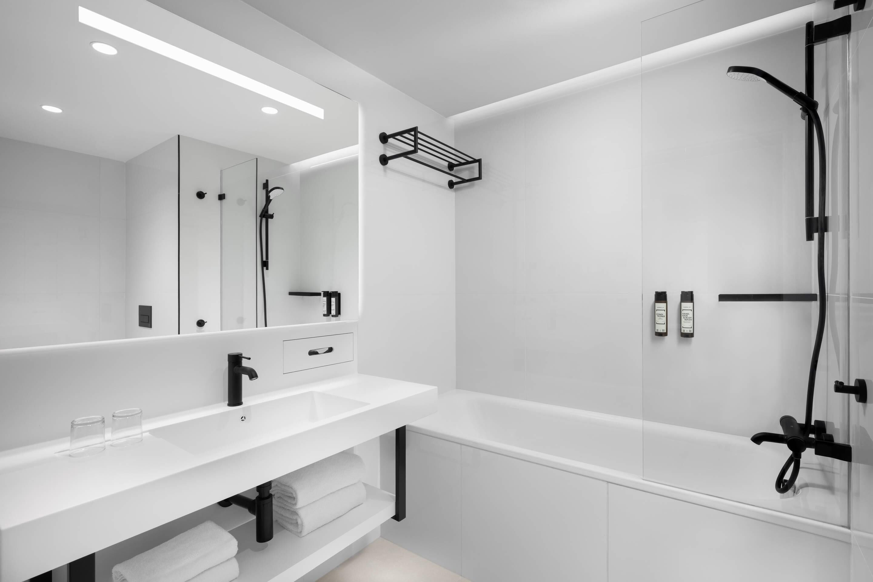 Un baño moderno con un tocador blanco, un espejo grande, una ducha con cabezal de ducha manual y un perchero para toallas.