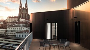 Un bâtiment moderne doté d’un balcon agrémenté de deux chaises et d’une table, offrant une vue sur une église historique et le paysage urbain.