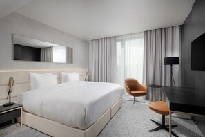 Une chambre d’hôtel moderne avec un grand lit, un bureau, une chaise et un téléviseur.