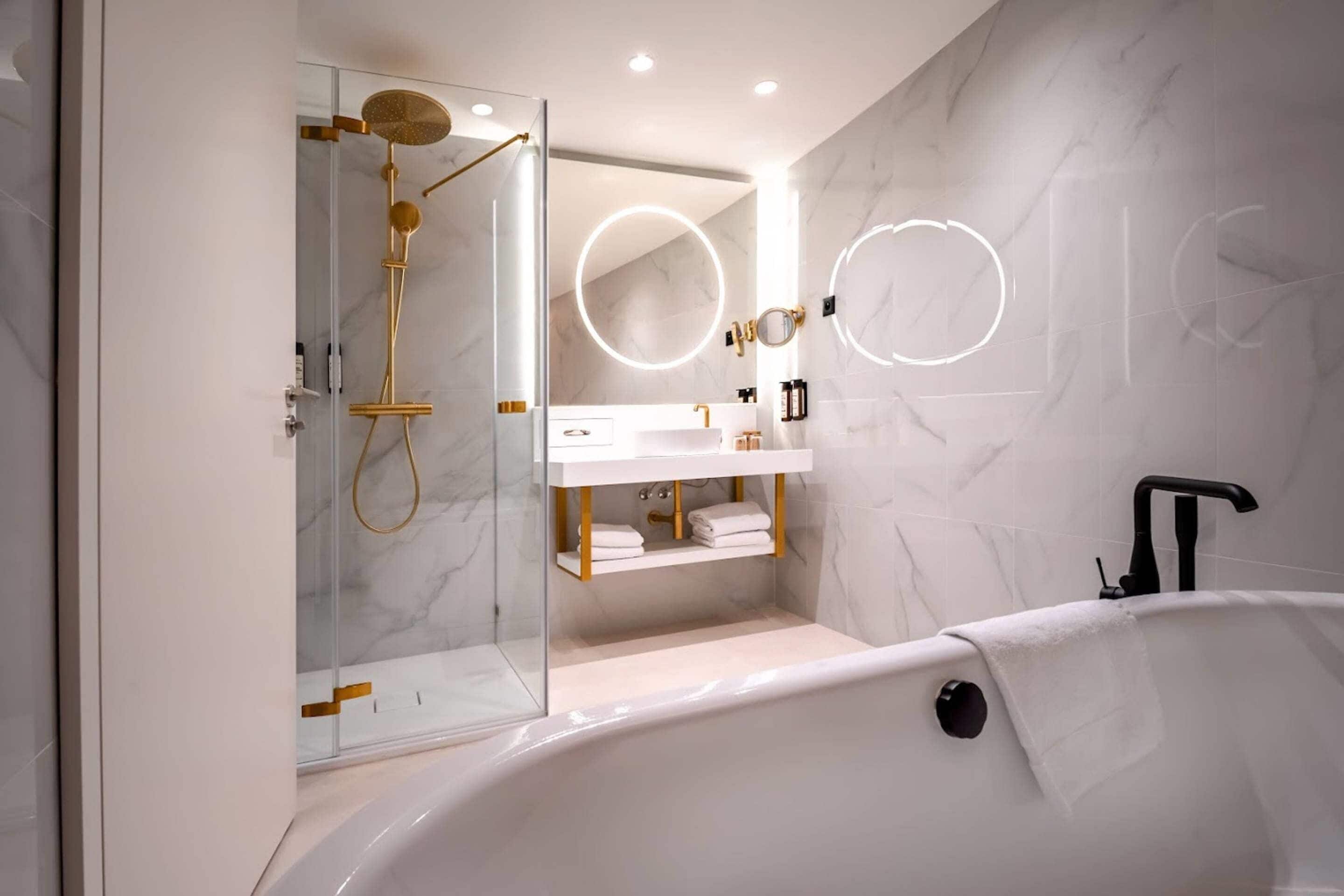 A modern bathroom with a glass-enclosed shower, a white vanity with gold fixtures, and a large bathtub.