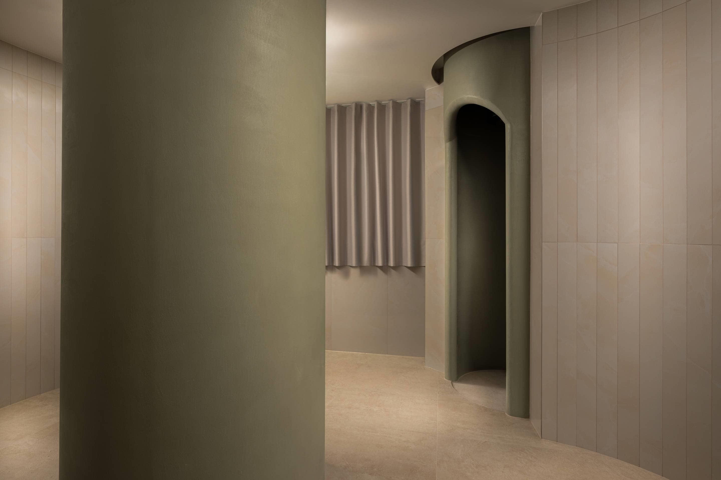 Un pasillo con una pared curva, una columna y una ventana con cortinas.
