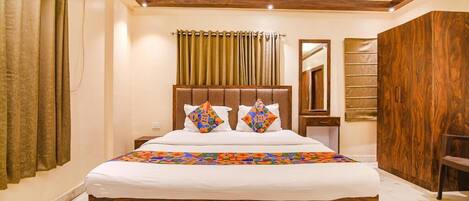 A bedroom with a wooden headboard, a bed with patterned pillows, a bedside table, a mirror, and a wardrobe.